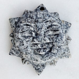 May include: A grey stone sun with a smiling face carved into it. The sun has a starburst shape with 12 points.
