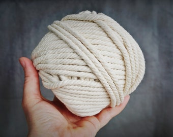 May include: A ball of natural white cotton rope, held in a hand. The rope is tightly wound and has a smooth texture.