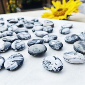 May include: A collection of oval-shaped, black and white marbled beads. The beads are smooth and glossy, with a swirling pattern.