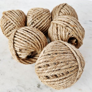 May include: A group of six balls of natural brown twine, made from jute, are arranged on a white marble surface.