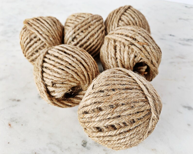 May include: A group of six balls of natural brown twine, made from jute, are arranged on a white marble surface.