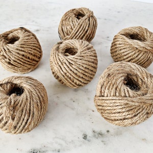 May include: Six balls of natural brown twine, each wound into a tight ball, are arranged on a white marble surface.