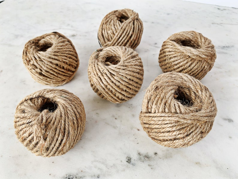May include: Six balls of natural brown twine, each wound into a tight ball, are arranged on a white marble surface.