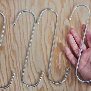 May include: Five silver S-shaped hooks with rounded ends. The hooks are hanging on a wooden surface.