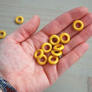 May include: A hand holding a group of yellow wooden rings. The rings are approximately 2.5 cm in diameter and have a smooth finish.