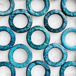 以下が含まれることがあります： 白の表面に、滑らかで光沢のある仕上げのティールブルーの丸いセラミックリングが円形に配置されています。