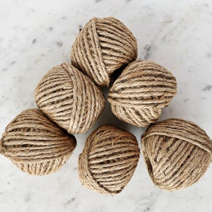 May include: Six balls of natural brown twine, arranged in a triangular shape on a white marble surface.