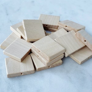 May include: A pile of unfinished, square wooden blocks with a hole drilled through the centre of each block. The blocks are light brown in colour.