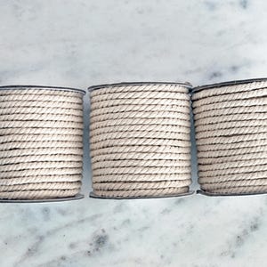 May include: Three spools of natural colored cotton rope, each wound tightly and ready for crafting projects.