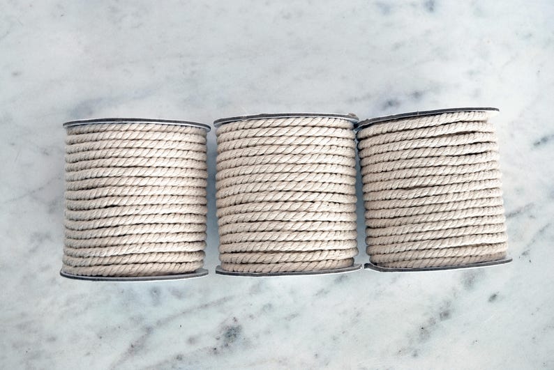 May include: Three spools of natural colored cotton rope, each wound tightly and ready for crafting projects.