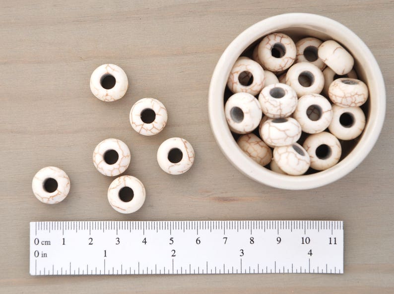 K&ouml;nnte beinhalten: Eine Schale mit wei&szlig;en Holzperlen mit braunen Marmorierungen. Die Perlen haben ein gro&szlig;es Loch in der Mitte und haben einen Durchmesser von etwa 2,5 cm.