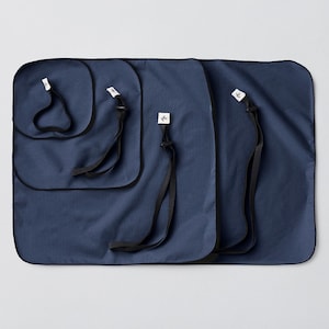 Puede incluir: Cuatro bolsas de almacenamiento de tela azul con correas negras y etiquetas blancas. Las bolsas están anidadas una dentro de la otra, con la bolsa más grande en la parte inferior y la bolsa más pequeña en la parte superior.