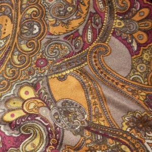 May include: Paisley print pants in shades of gold, burgundy, and brown. The fabric has a silky sheen and a detailed, ornate pattern. The pants are folded, showing the full design.