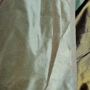 May include: Close-up of a dark green fabric with a subtle sheen. The fabric has a smooth texture with visible folds and creases, creating shadows and highlights. The edge of the fabric is visible, showing a finished seam.