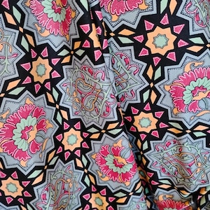 May include: A fabric featuring a repeating geometric pattern of eight-pointed stars and floral motifs in shades of magenta, light green, peach, and grey, set against a black background. The design includes intricate scrollwork and dotted details.