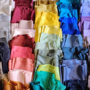 May include: A collection of folded fabric in various colors, including white, red, yellow, blue, and green. The fabrics are neatly arranged, showcasing a spectrum of hues and textures, suitable for sewing or crafting projects.