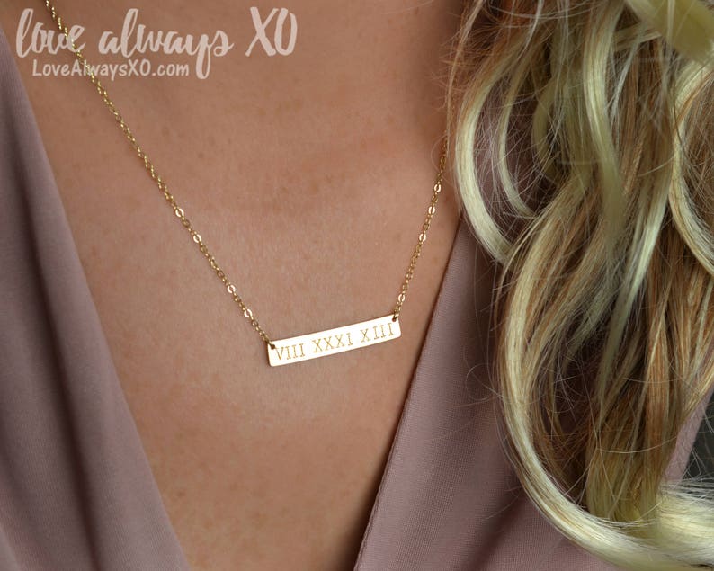 Peut inclure: Un collier dor&eacute; avec une cha&icirc;ne d&eacute;licate. Le pendentif rectangulaire porte des chiffres romains. Le texte "Love always XO" et l'adresse du site web sont dans le coin sup&eacute;rieur gauche.