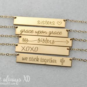 Peut inclure: Colliers dor&eacute;s avec des barres grav&eacute;es de texte. Les colliers indiquent "sisters", "grace upon grace", "sisters", "XOXO" et "we stick together". Chaque barre est reli&eacute;e &agrave; une cha&icirc;ne d&eacute;licate.