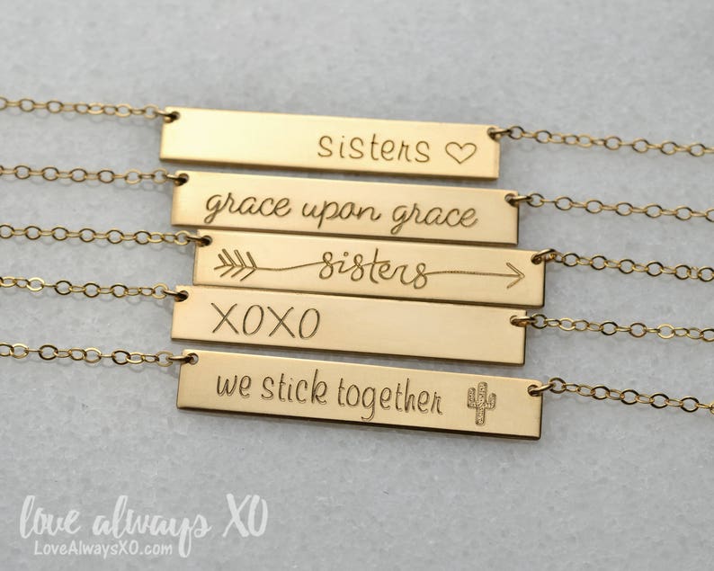 Peut inclure: Colliers dor&eacute;s avec des barres grav&eacute;es de texte. Les colliers indiquent "sisters", "grace upon grace", "sisters", "XOXO" et "we stick together". Chaque barre est reli&eacute;e &agrave; une cha&icirc;ne d&eacute;licate.