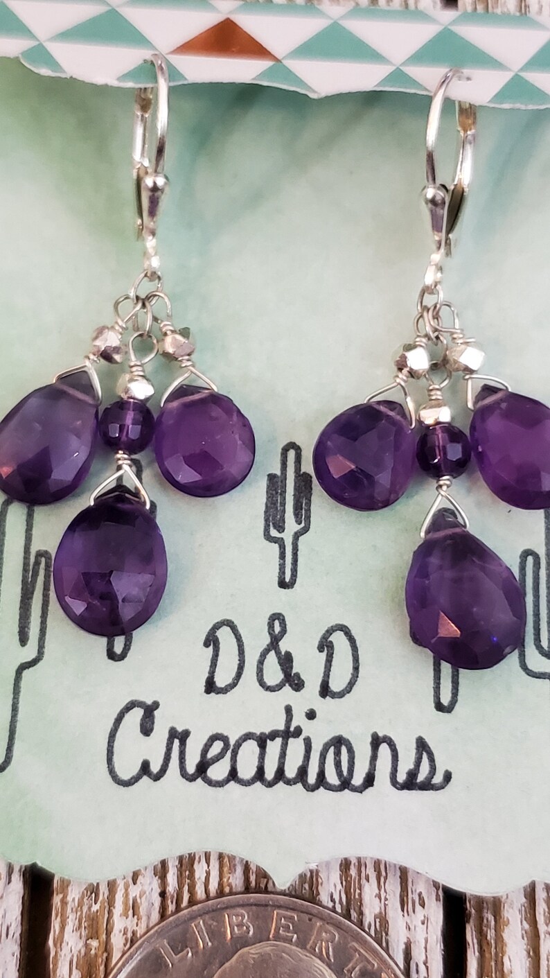 K&ouml;nnte beinhalten: Ein Paar Ohrh&auml;nger mit facettierten, tiefvioletten Amethyst-Tropfen- und runden Perlen. Die Ohrringe sind an silberfarbenen Klappb&uuml;gelverschl&uuml;ssen befestigt. Im Hintergrund ist der Text "D & D Creations" zu sehen.