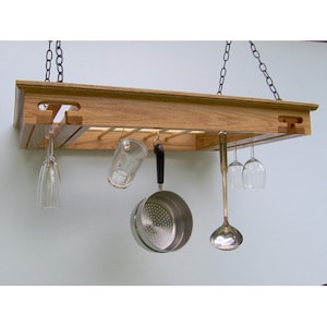 May include: A wooden hanging shelf with a slatted design, featuring hooks for hanging kitchen utensils and wine glasses. The shelf is made of natural wood and has a rustic look.