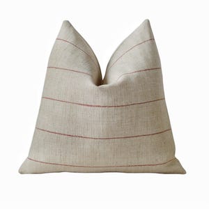 May include: A beige linen pillow with horizontal red stripes. The pillow has a soft, textured appearance and a classic design. This decorative pillow is suitable for a bed or sofa.