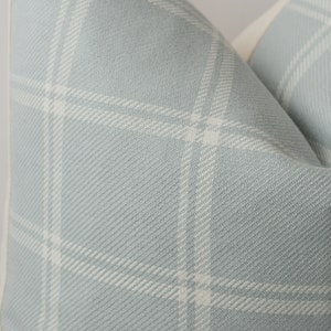 May include: Close-up of a light blue pillow with a white plaid pattern. The pillow has a white border.