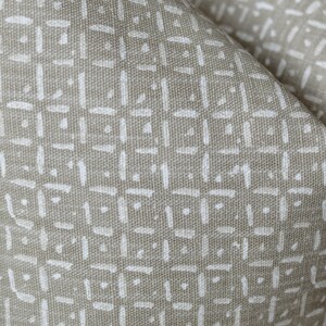 Peut inclure: Gros plan sur un tissu beige avec un motif g&eacute;om&eacute;trique blanc. Le motif est compos&eacute; de petites lignes fines qui cr&eacute;ent un design en forme de grille.