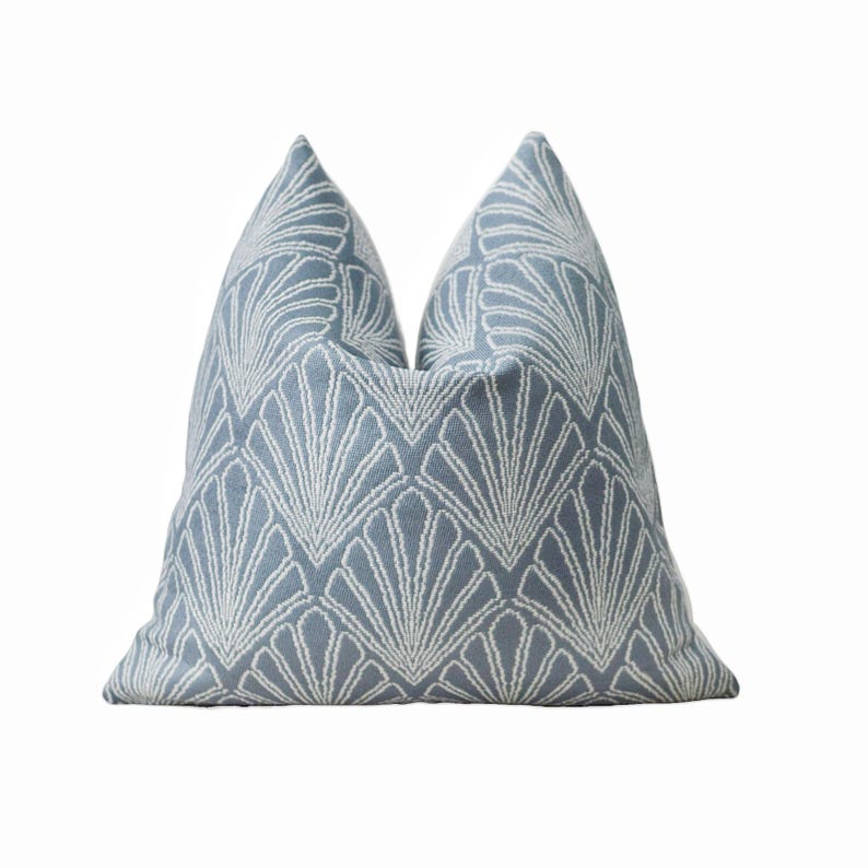 May include: A decorative throw pillow with a light blue background and a white, fan-shaped pattern. The pillow has a textured appearance and is designed for home decor.