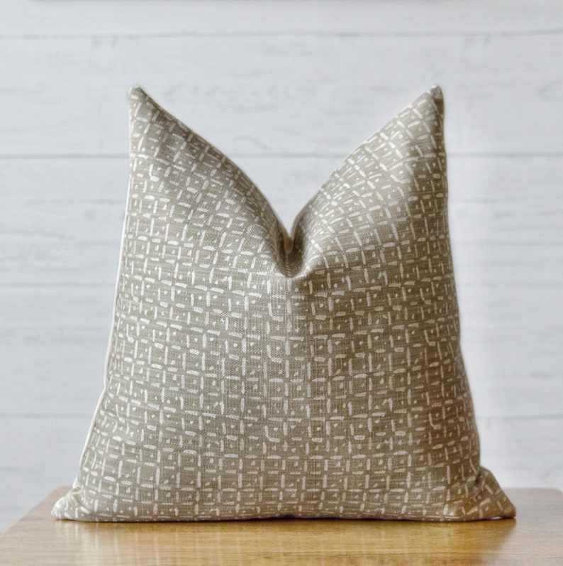 Peut inclure: Un coussin beige avec un motif g&eacute;om&eacute;trique blanc. Le coussin est fait d'un tissu doux et textur&eacute;.