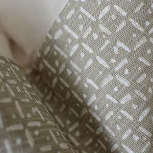 Peut inclure: Gros plan sur un tissu beige avec un motif g&eacute;om&eacute;trique blanc. Le tissu a une surface textur&eacute;e et un l&eacute;ger brillant.