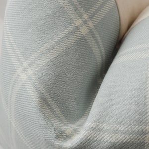 May include: Close-up of a light blue fabric with a white plaid pattern. The fabric is soft and textured, with a subtle sheen.
