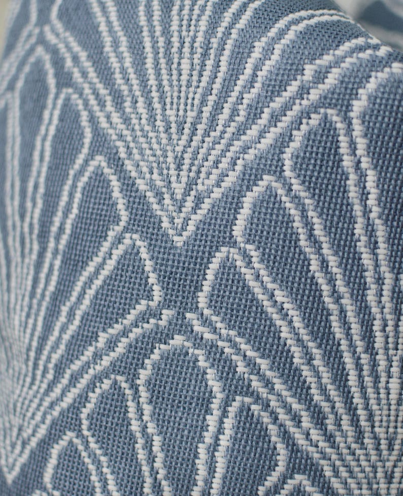 May include: Close-up of a blue and white woven fabric. The fabric features a repeating geometric pattern of white lines against a blue background. The texture appears to be a tight weave, suggesting a durable material suitable for upholstery or home decor.