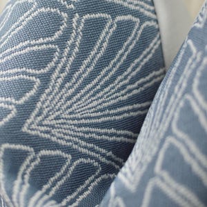 May include: Close-up of a blue and white patterned fabric. The fabric has a woven texture with a repeating design of stylized leaf shapes. The color is a muted blue with white accents, creating a soft, textured appearance.