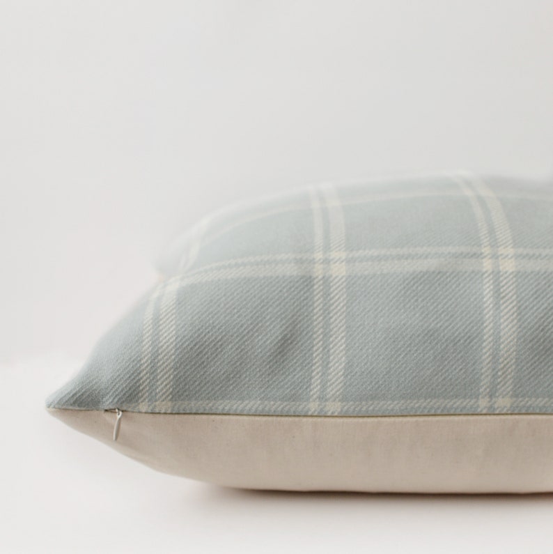May include: A light blue throw pillow with a white plaid pattern. The pillow has a hidden zipper closure and a cream-colored backing.