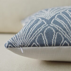 May include: Close-up of a decorative pillow with a blue and white geometric pattern. The pillow has a white zipper and a neutral-colored base. The pattern is a repeating design of white lines on a blue background. The pillow is made of a textured fabric.