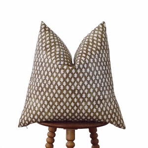 May include: A brown and white patterned throw pillow with a geometric design. The pillow is sitting on a wooden stool.