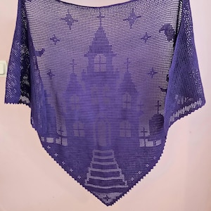 Könnte beinhalten: Ein dreieckiges, violettes Häkeltuch mit einem komplexen Lochmuster, das die Silhouette einer gotischen Burg mit hohen Türmen, Rundbogenfenstern und einem zentralen Tor zeigt, verziert mit kleinen, über den Stoff verteilten Sternen.