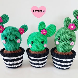 Puede incluir: Tres cactus de peluche tejidos a crochet en macetas rayadas en blanco y negro con flores rosas. Los cactus tienen caras sonrientes y cuerpos verdes.