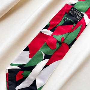 Puede incluir: Una corbata con un patrón gráfico llamativo de grandes formas rojas, verdes y blancas sobre un fondo negro. En la parte posterior hay una etiqueta negra cosida que dice: GRAVATES PIERRE CARDIN MODÈLE PARIS DÉPOSÉ MADE IN FRANCE.