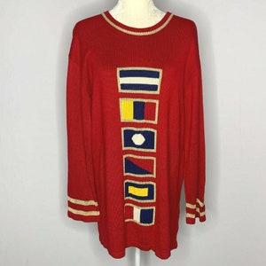 May include: Red long-sleeved sweater with a vertical row of colorful nautical flags on the front. The sweater has gold trim around the neckline and cuffs.