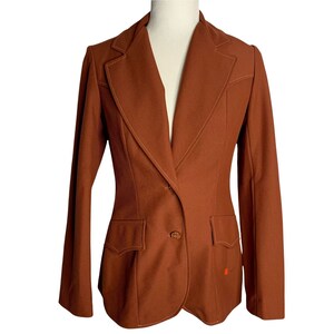 Può includere: Un blazer marrone con una chiusura a un bottone e due tasche a lembo. Il blazer ha un colletto a revers e una vestibilità slim.