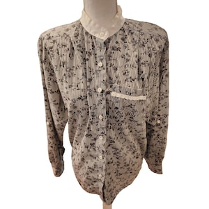 May include: A white and black striped long-sleeve button-up shirt with a floral print. The shirt has a white collar with a lace trim and a small pocket on the left chest.