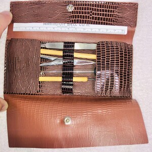 May include: Open brown faux-leather case with a reptile skin texture, containing various tools and a ruler. The case is secured with a snap closure. The ruler has the text "HAMILTON BELL CO. INC." printed on it.