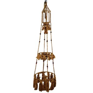 May include: A three-tiered macrame plant hanger with brown rope and wooden beads. The hanger has three circular shelves with fringe details.