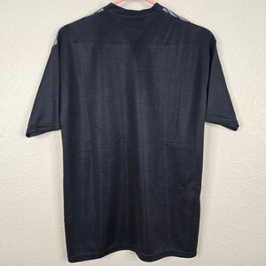 May include: Black short-sleeved athletic shirt with a high neckline and gray accents on the shoulders. The shirt is hanging on a pink hanger against a plain white background. The fabric appears to be a breathable, athletic material.