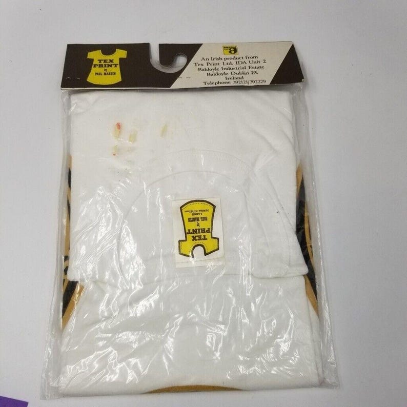 May include: A white t-shirt in a clear plastic bag with a cardboard header. The header has the text "TEX PRINT" and a logo. The shirt has a small tag with the text "TEX PRINT" on it.