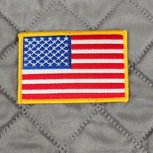 以下が含まれることがあります： 黄色の縁取りが付いた、小さな刺繍されたアメリカ国旗のパッチ。旗は赤、白、青です。