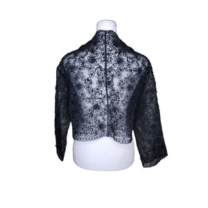 May include: A black lace shrug with a floral pattern. The shrug is cropped and has three-quarter sleeves.
