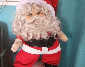 Puede incluir: Un muñeco de peluche de Papá Noel con barba blanca y traje rojo y blanco. El muñeco lleva un gorro rojo con ribete blanco.